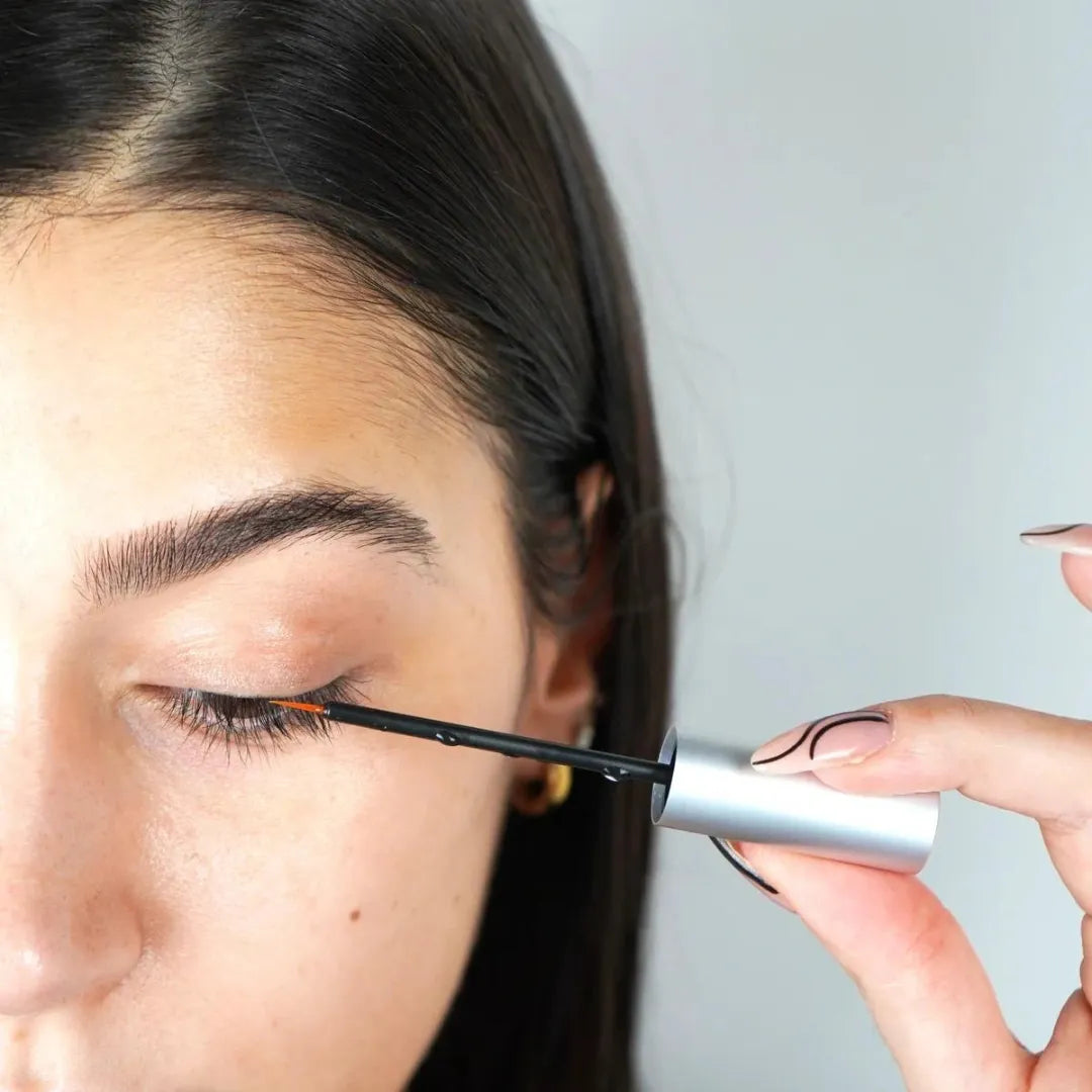 Close up of woman putting on lash serum with wand