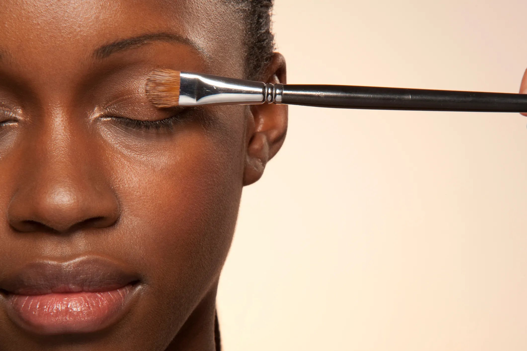 Woman with eyes closed holding a makeup brush near her eye