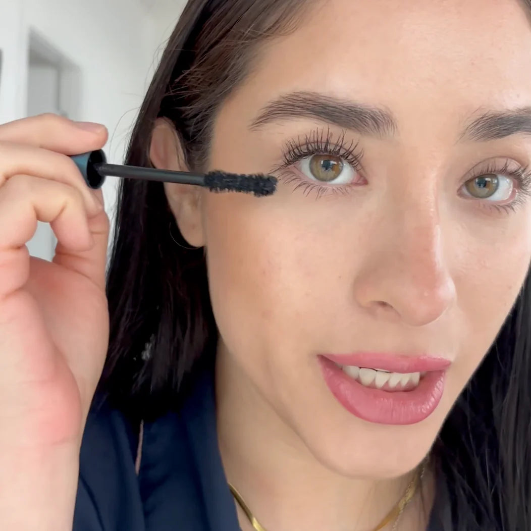 Woman applying mascara to her eyelashes with a close-up focus on her face.