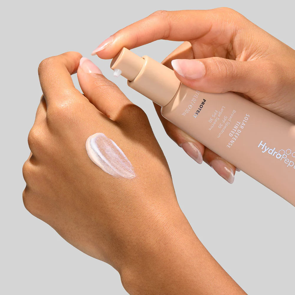 Hand applying a skincare product to another hand with a neutral background