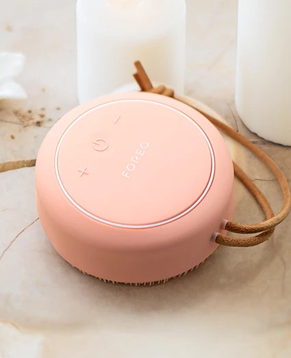 Pink portable FOREO body massager with a rope on a light surface