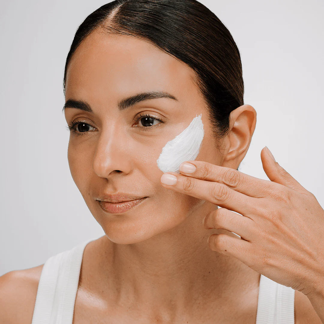 Woman applying cream to her face with a neutral background