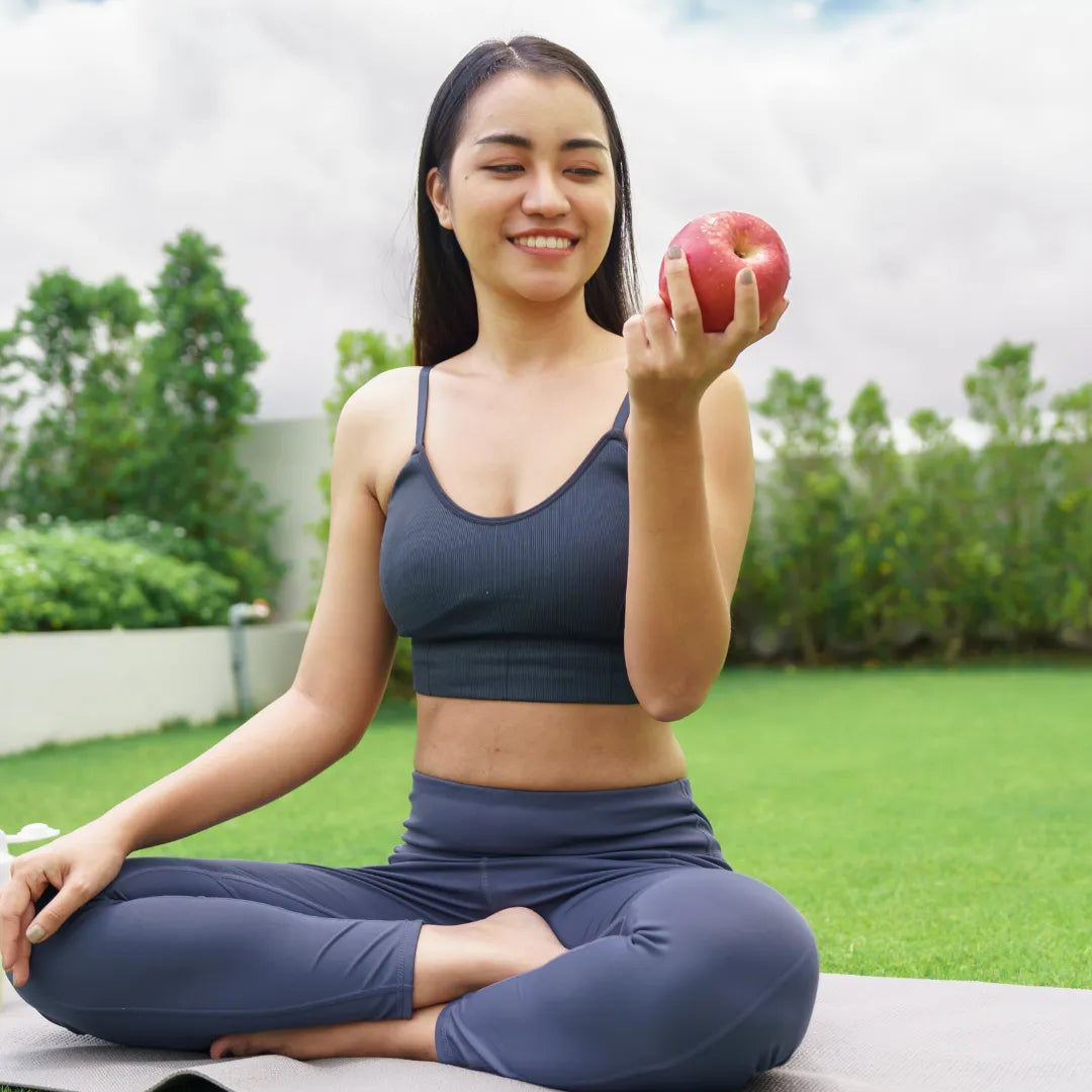 woman holding an apple sitting on yoga mat