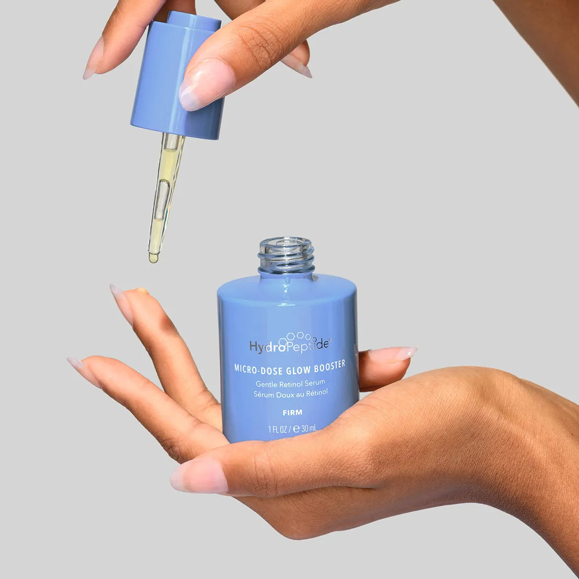 Blue skincare serum bottle with dropper held by a hand against a gray background
