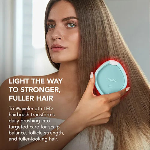 A woman with long light brown hair holds a light blue FOREO tri-wave LED hairbrush against her hair, with promotional text on the left side of the image.