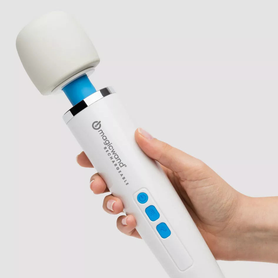 A hand holding a Magic Wand Rechargeable personal massager against a light gray background. The device is primarily white with bright blue buttons and accents, and a black printed logo on the handle.