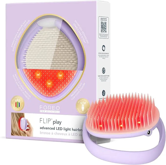 FOREO FLIP play advanced LED light hairbrush shown with its lavender retail box on a white background. The hairbrush has a lavender handle and bristles, with the LEDs illuminated in red/orange, and the packaging displays a large circular view of the product.