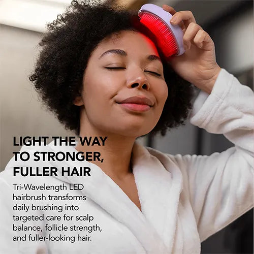 A woman in a white robe uses a tri-wave LED hairbrush on her scalp, with text overlay reading 'LIGHT THE WAY TO STRONGER, FULLER HAIR'.