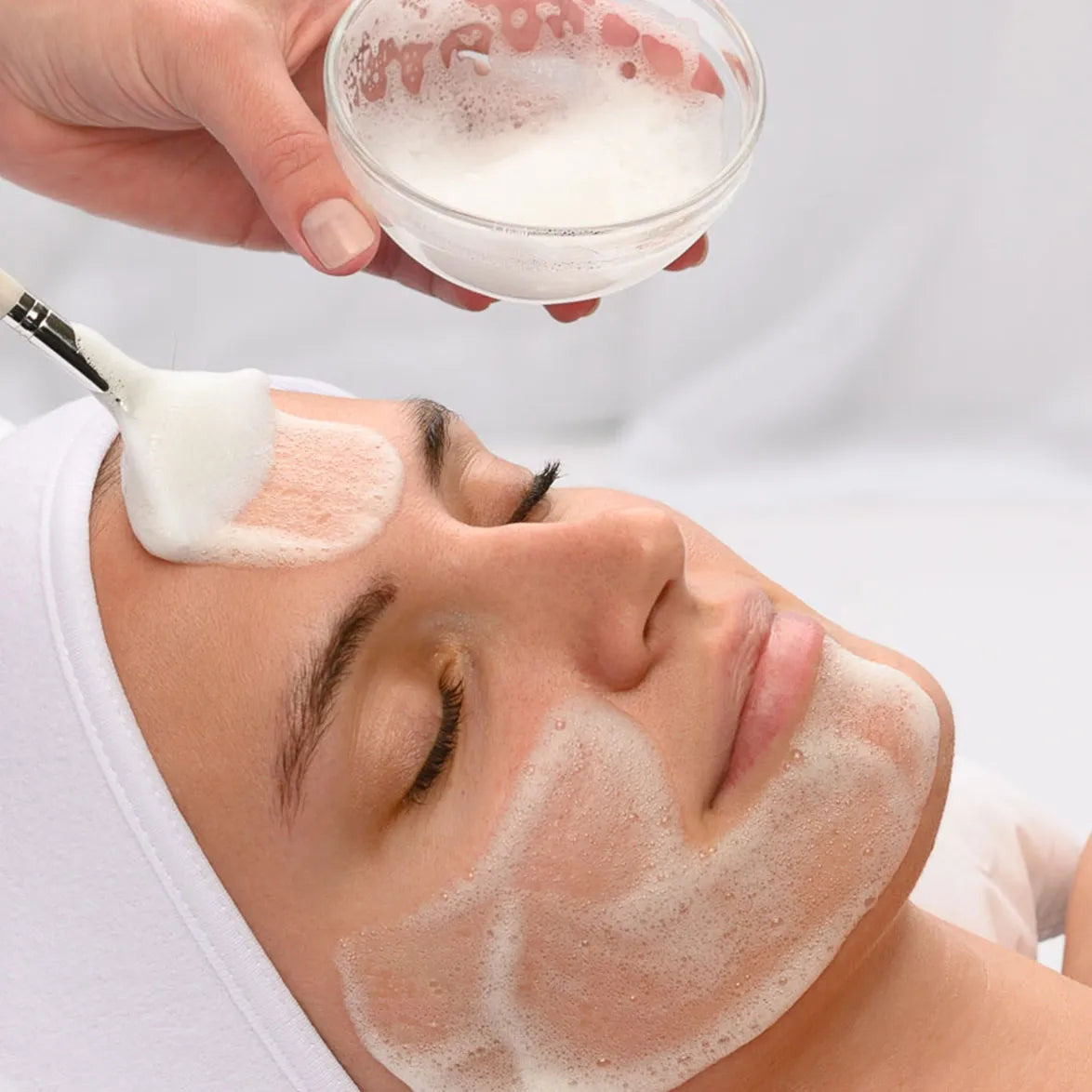Person applying a facial mask to their face with a brush.