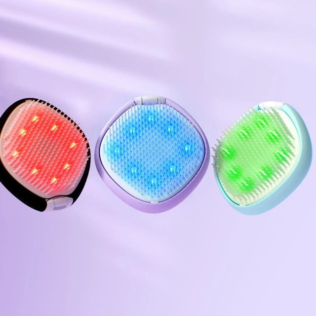 Three handheld LED light therapy scalp massage devices shown side by side on a soft lavender background. The left device is black with a glowing red LED panel, the middle is lavender with a blue LED panel, and the right is mint green with a light green LED panel.