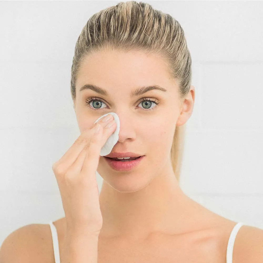 Woman applying pad to her face with a white background