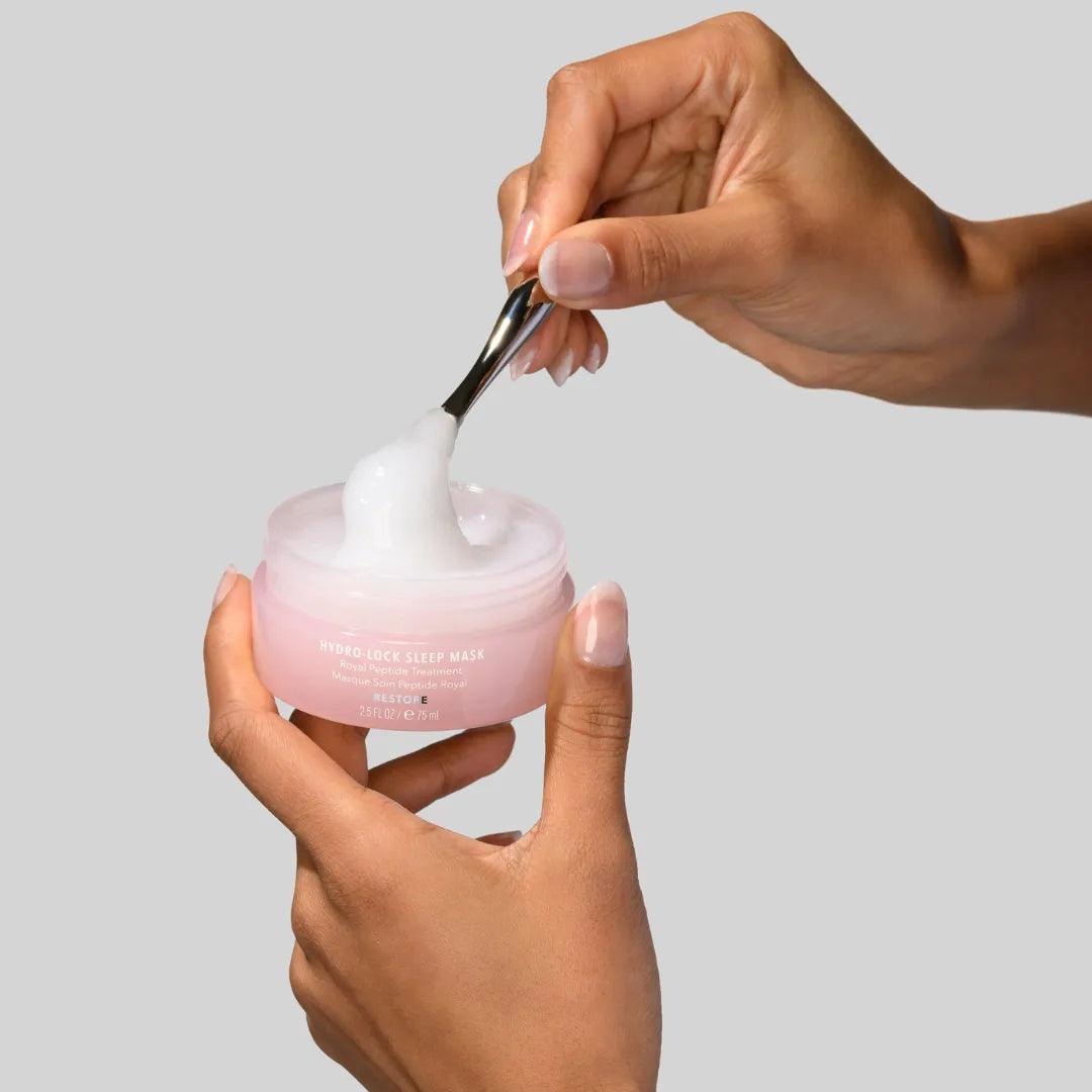 Person applying pink cream from a jar with a spoon on a gray background