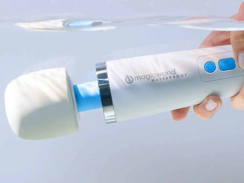 Hand holding a white and blue electronic device labeled 'magicwand' on a light gray background
