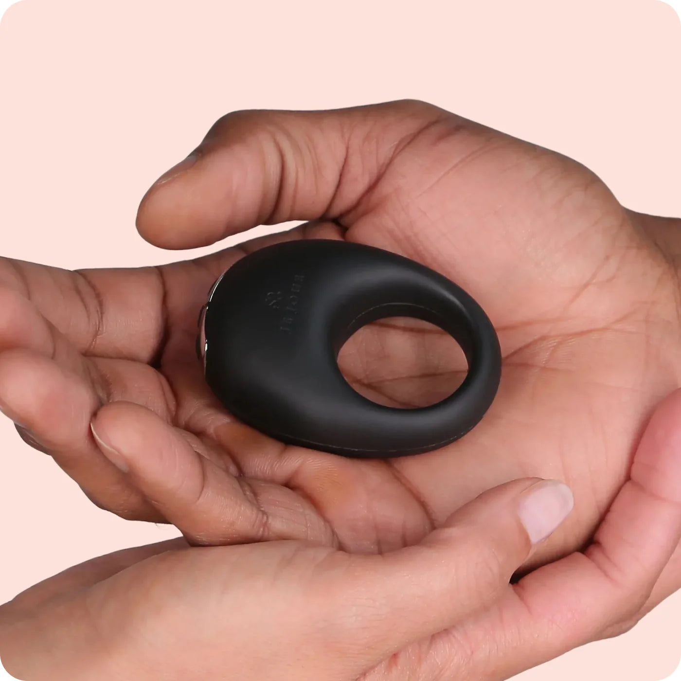 Black ring held in a hand against a light pink background