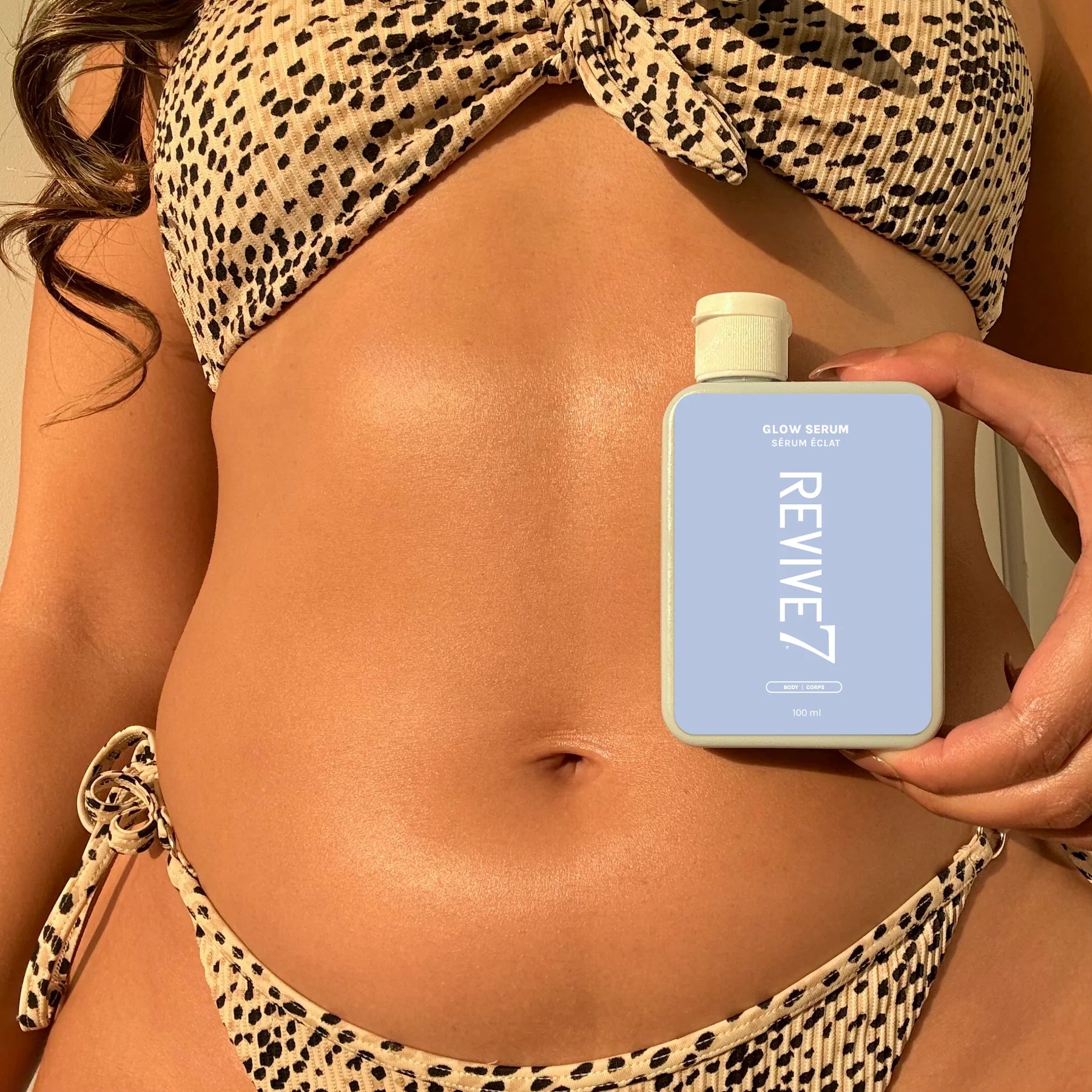 Person holding a 'REVIVE7' product bottle with leopard print bikini