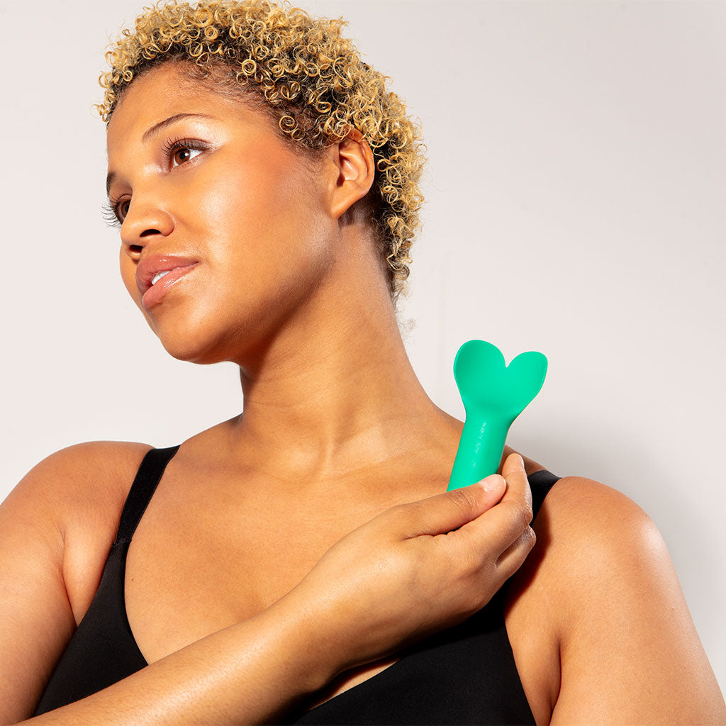 Woman holding a green heart-shaped object against a plain background