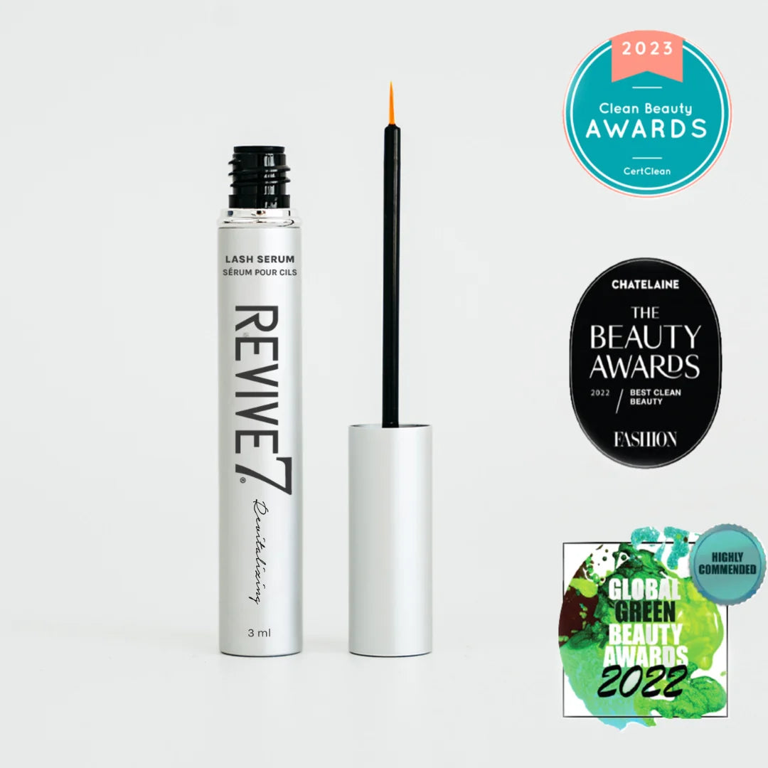 Revive7 Lash Serum in a silver and black bottle with its applicator wand shown beside it on a light gray background. Multiple award badges are displayed on the right, including Clean Beauty Awards 2023, The Beauty Awards 2023 Best Clean Beauty, and Global Green Beauty Awards 2022.