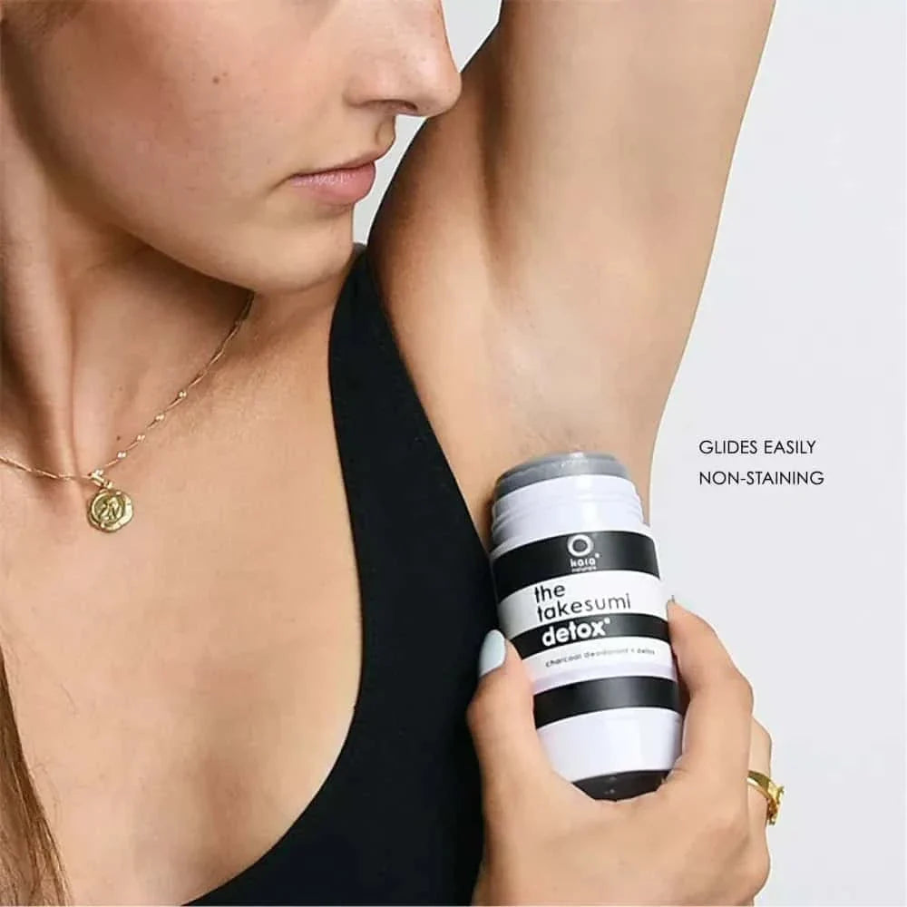 Person holding a can of 'the takesumi delox' deodorant near their arm against a white background