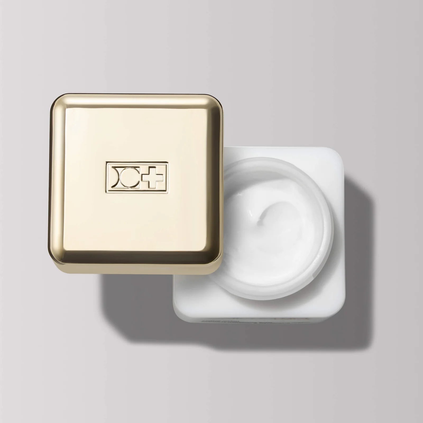Cosmetic container with gold lid and white cream on a gray background