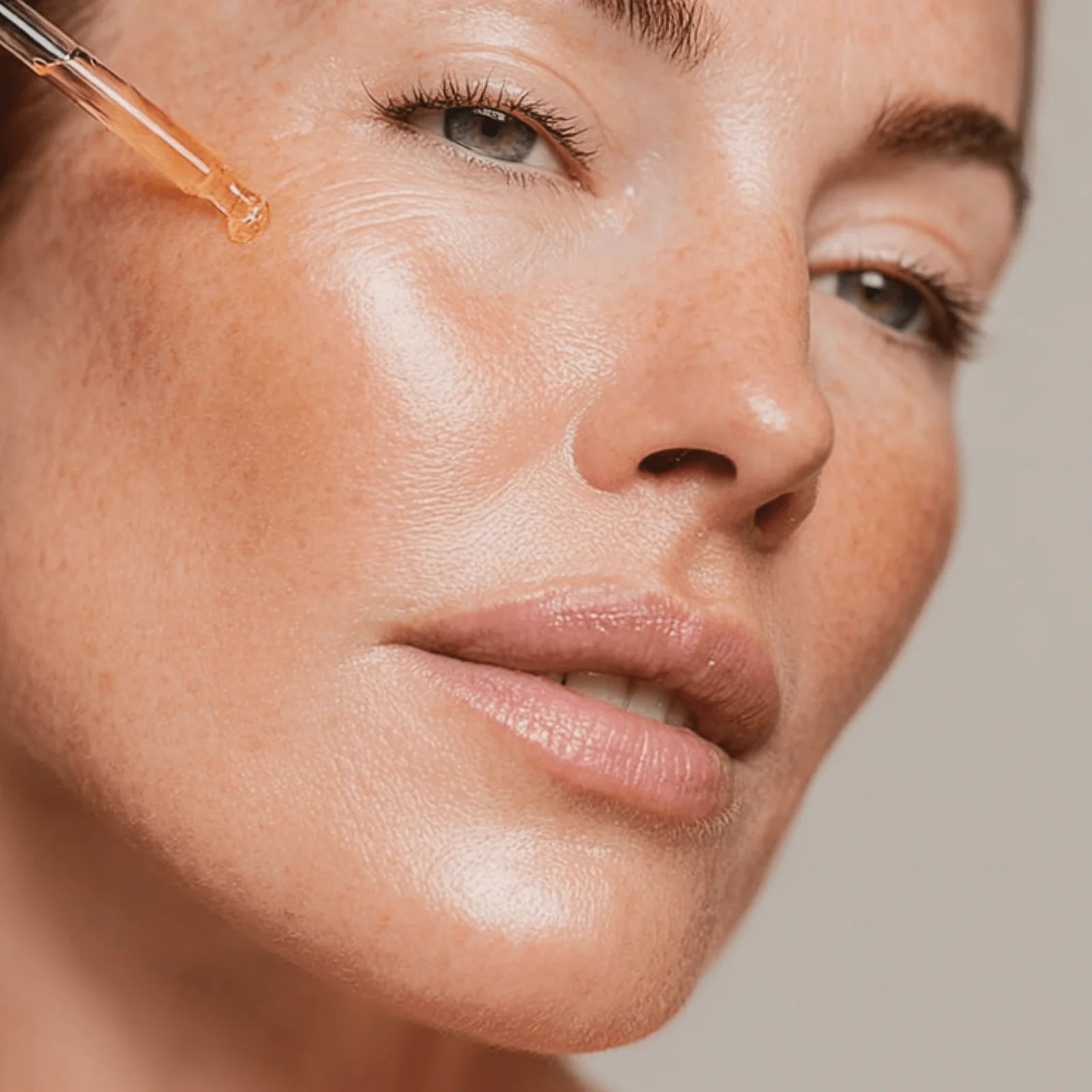 Close-up of a woman's face with a dropper applying a liquid to her skin.