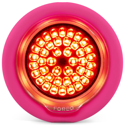 A circular pink LED light with a bright red illuminated face and multiple small LED bulbs, shown on a plain white background. The brand name FOREO is subtly visible at the bottom.