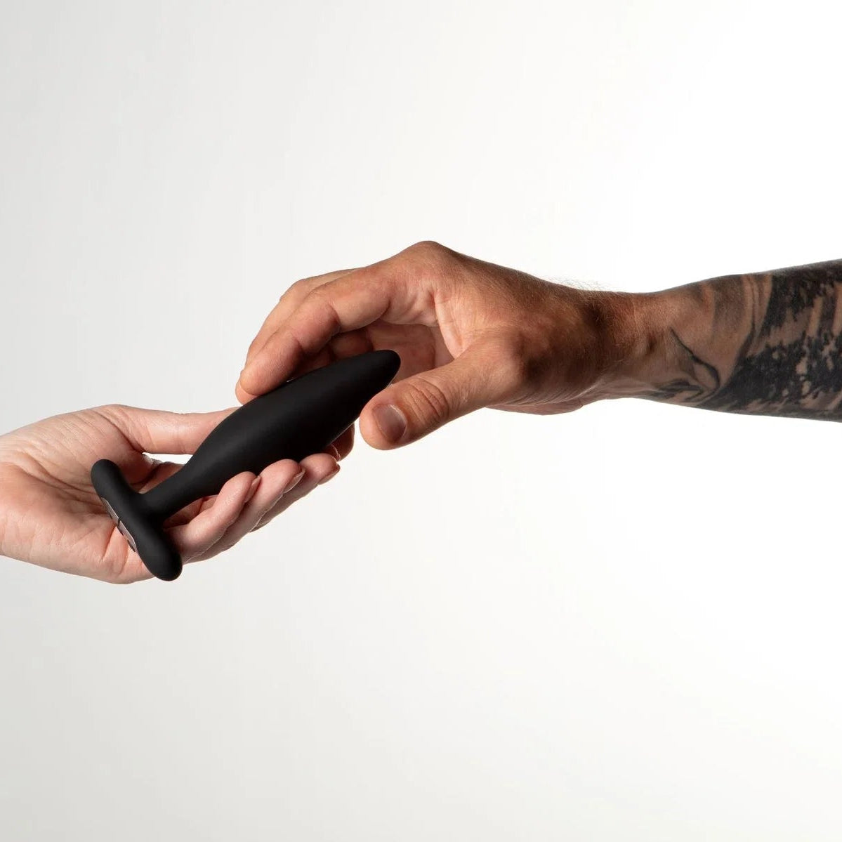 Two hands exchanging a black object against a plain background