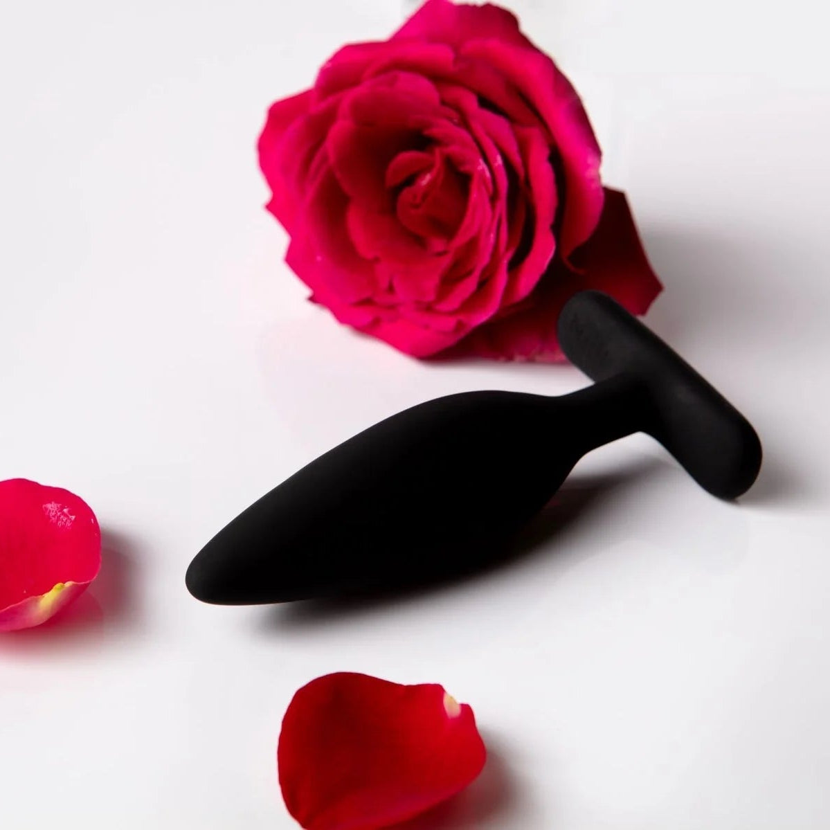 Black sex toy with a red rose and petals on a white background