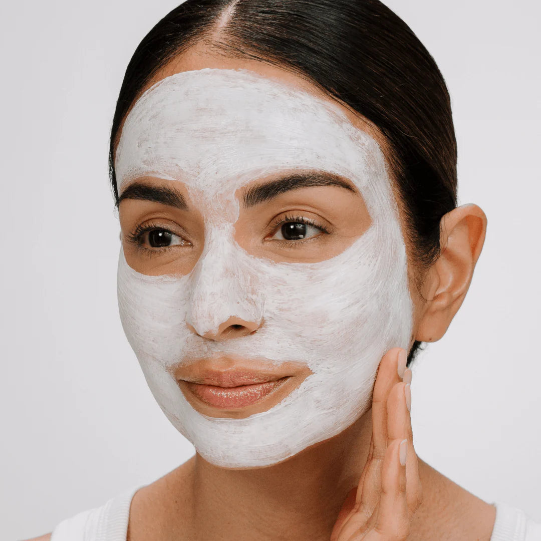 Woman applying a white facial mask on a plain background