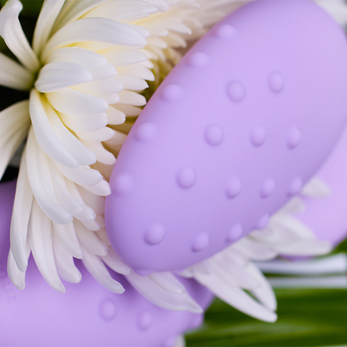 Purple egg-shaped massager with textured surface on a white flower background