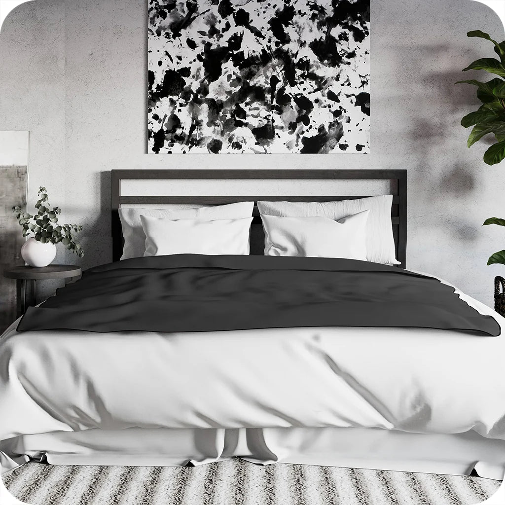 Bedroom with a bed featuring black and white bedding, abstract art on the wall, and plants.