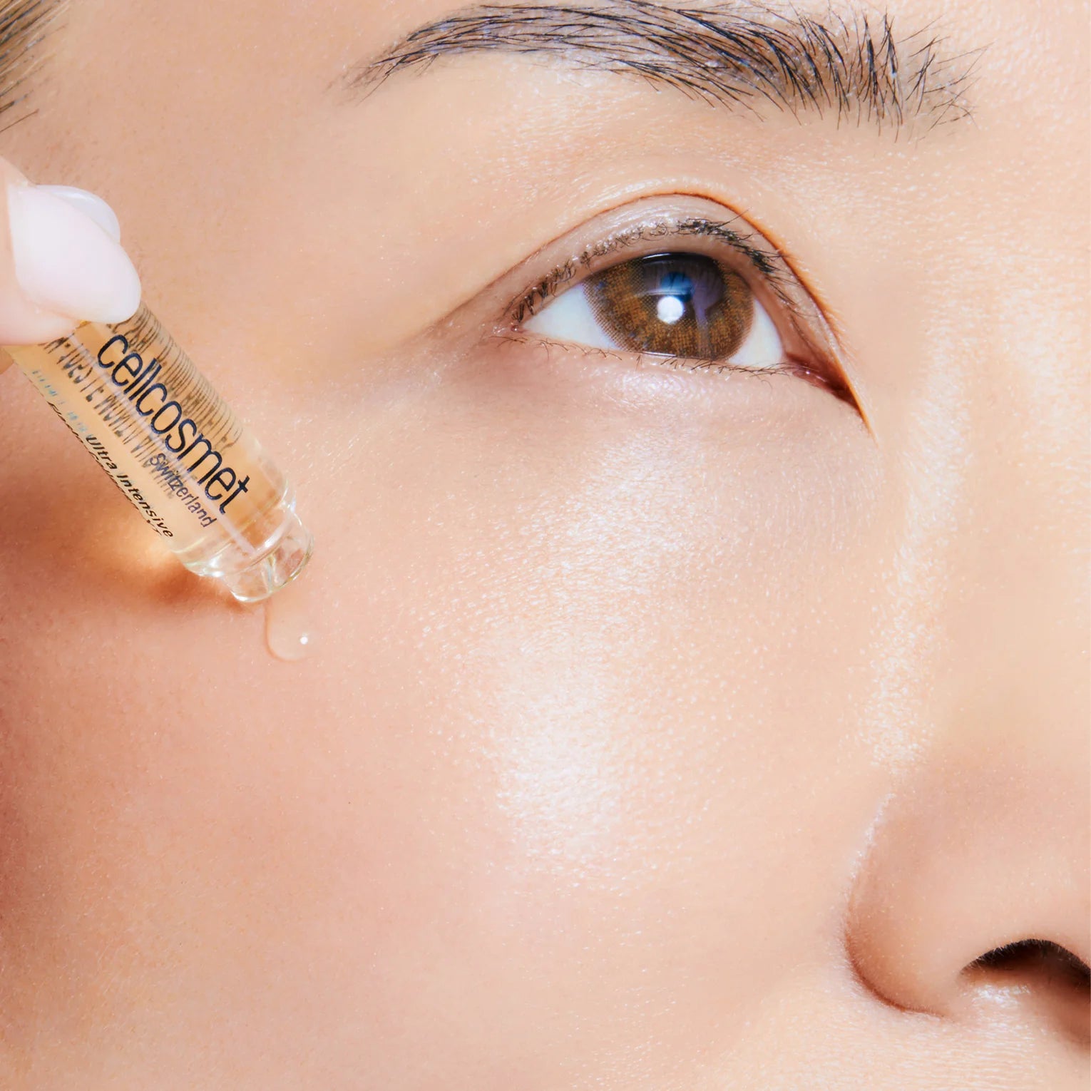 Close-up of a person applying a cosmetic dropper to their skin.