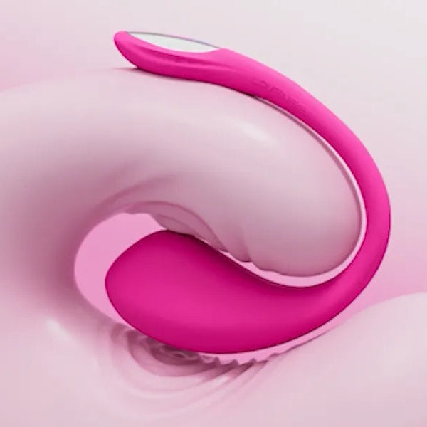 A close-up studio shot of a pink curved personal massager with a smooth matte finish, resting against a soft pink and white background.